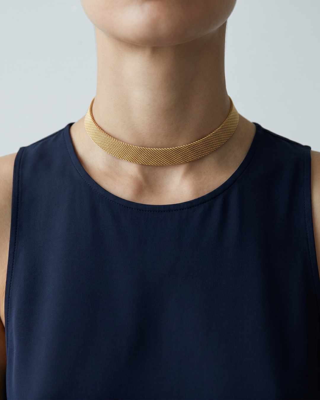 Mila mesh necklace worn at the base of the throat, gold-finished woven band catching the light