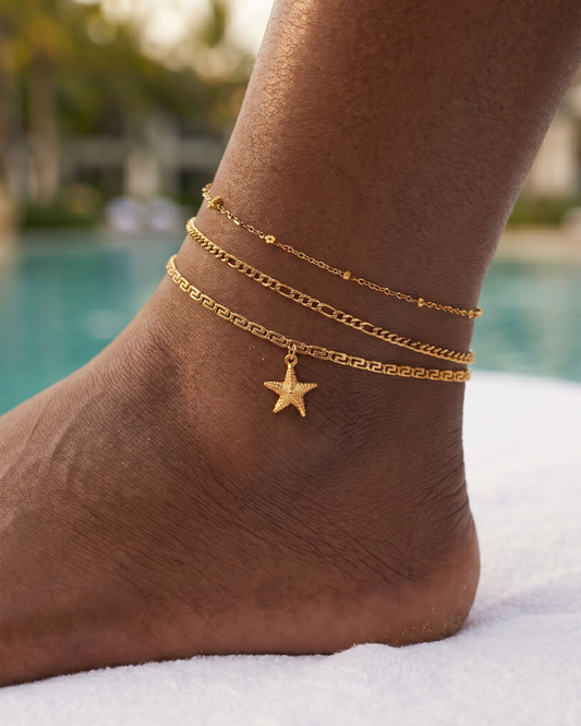 Algarve gold chain anklets with star charm worn on crossed feet on white sun lounger at luxury resort pool