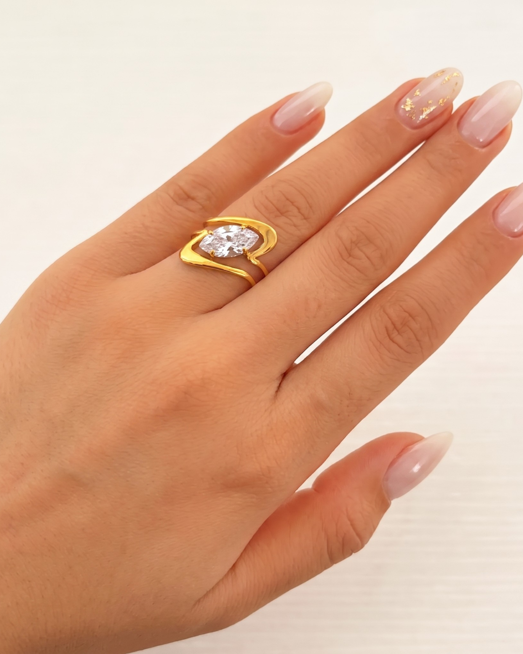Ondina ring worn on the finger, wave-form gold band with clear marquise stone