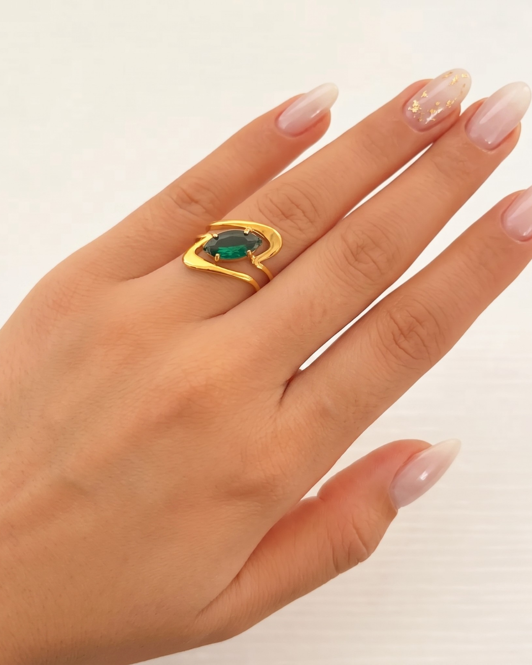 Ondina ring worn on the finger, wave-form gold band with emerald-green marquise stone