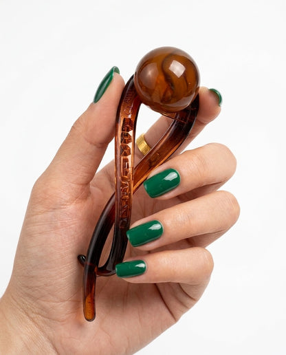 Suri twist bun holder in amber with creamy faux pearl bead, held to camera on neutral background
