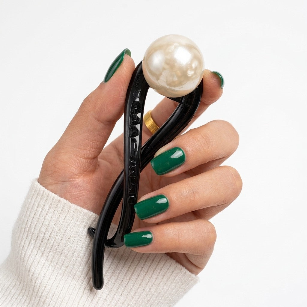 Suri twist bun holder in black with creamy faux pearl bead, held to camera on neutral backgroundon neutral background