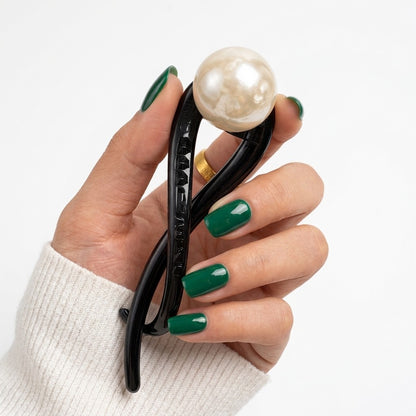 Suri twist bun holder in black with creamy faux pearl bead, held to camera on neutral backgroundon neutral background