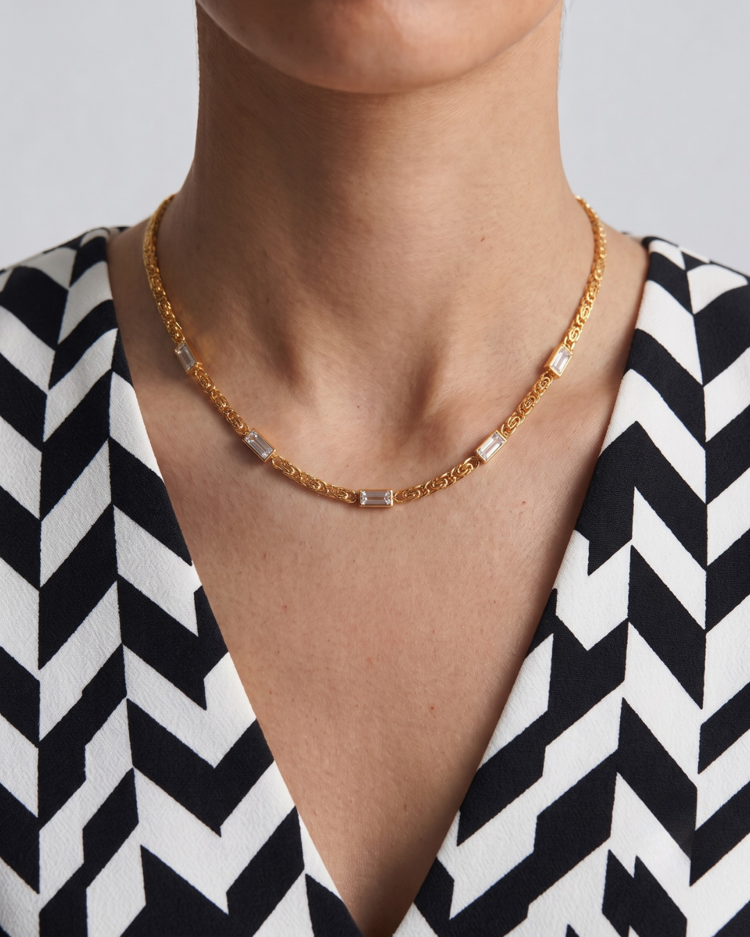 Thea necklace worn at the collarbone, flat scroll 18k gold plated chain with baguette crystal accents