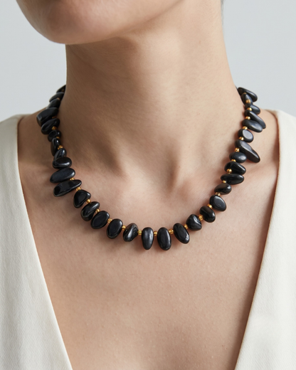 Tracy necklace in matte black worn at the collarbone, sculpted stone beads with gold accents