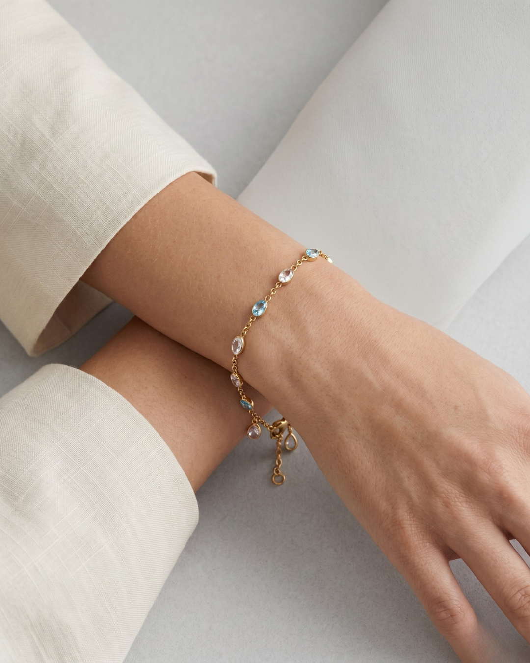 Woman wearing 18K gold chain bracelet with blue and white stone-effect drops on wrist, minimal white top, soft natural light — Tropea Bracelet by Clarabelle