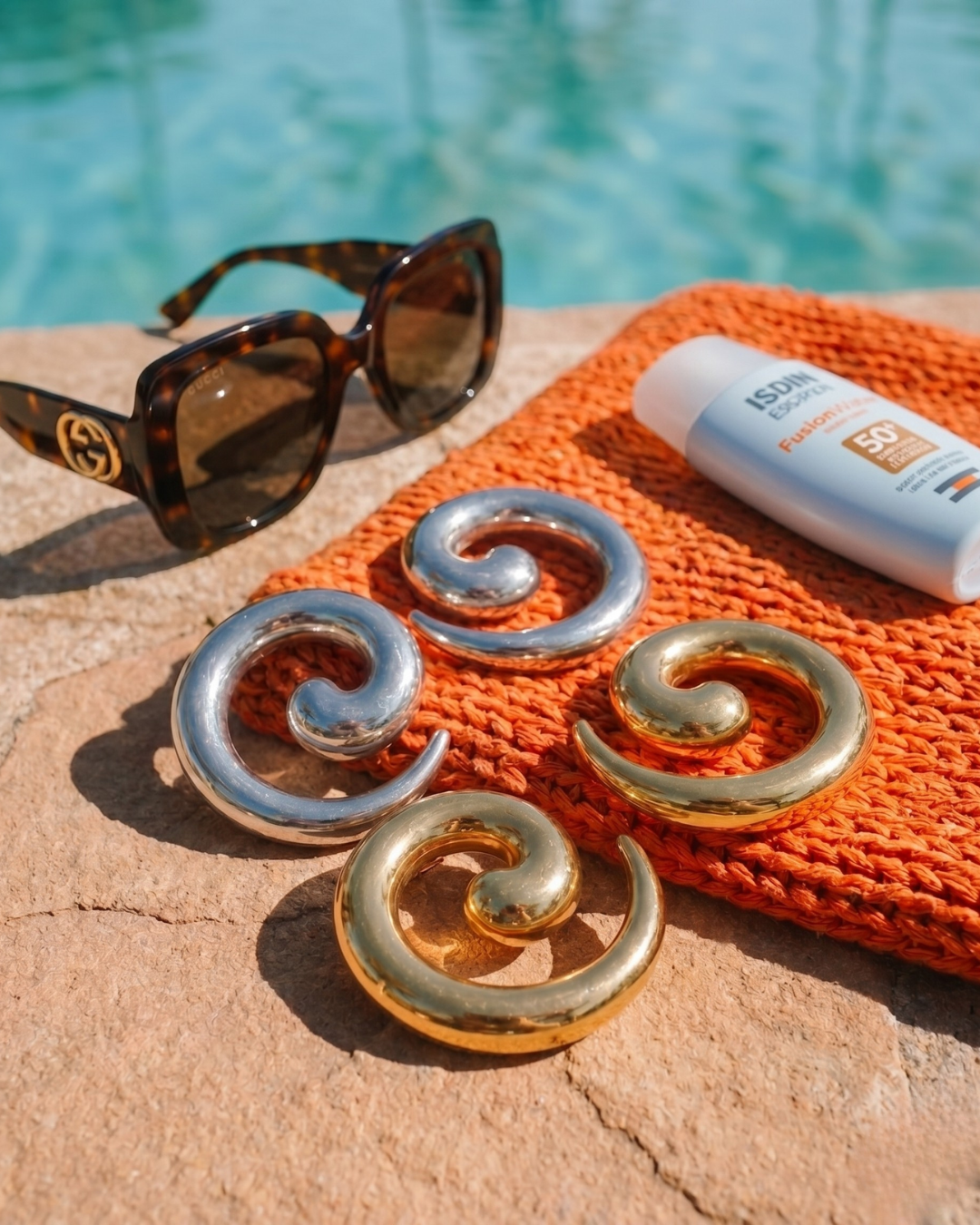 Gold and silver statement earrings placed poolside with sunglasses, summer jewellery styling