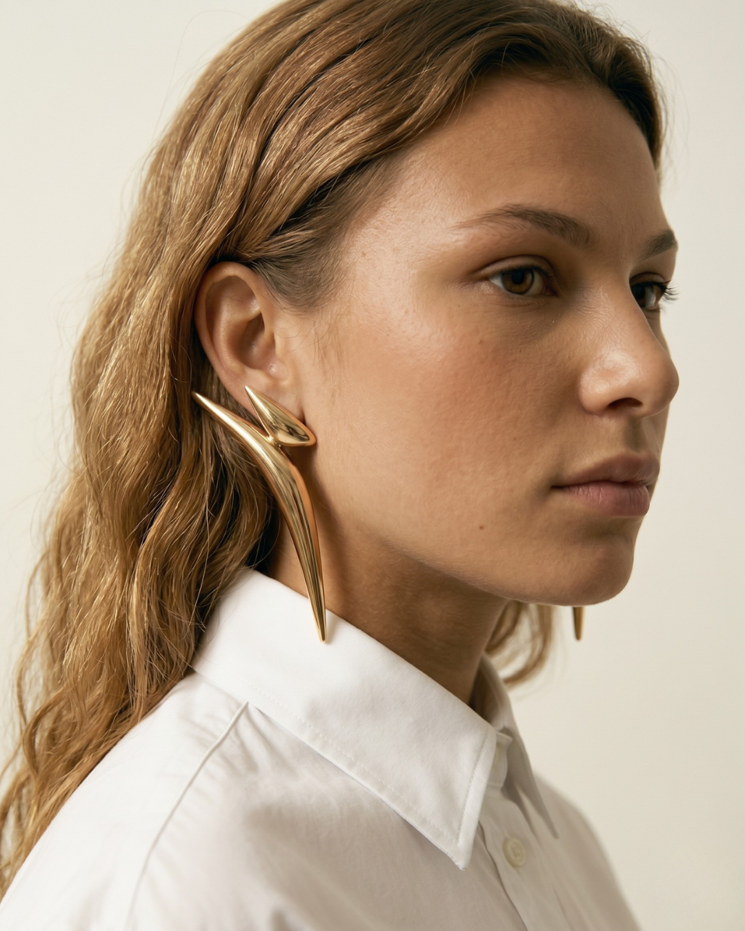 Close-up portrait of model wearing sculptural gold statement earrings