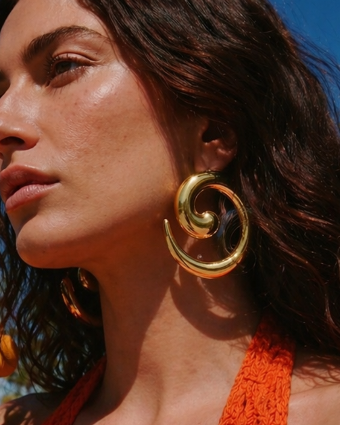 Close-up of model wearing gold statement earrings in sunlight, bold summer jewellery look