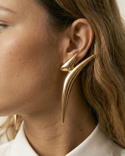 Detailed close-up of sculptural gold statement earrings worn by model