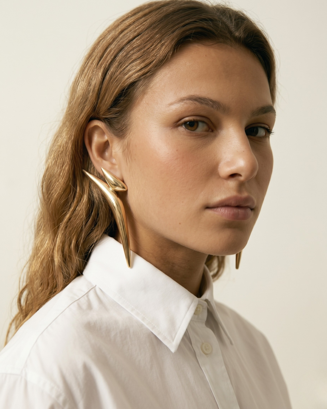 Fashion portrait of model wearing bold gold statement earrings by Clarabelle