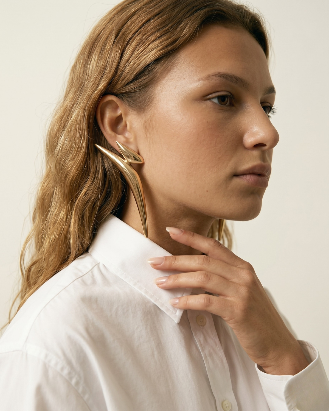 Model wearing long gold statement earrings with modern editorial styling