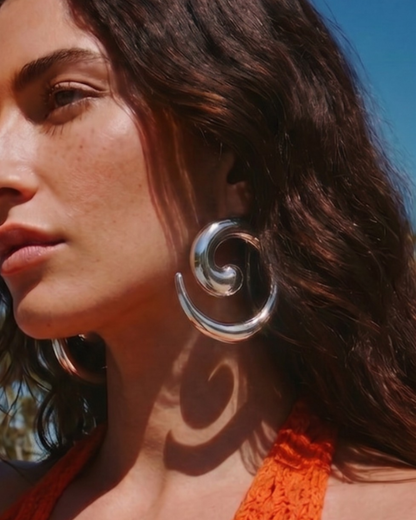 Close-up of model wearing silver statement earrings in sunlight, bold summer jewellery look