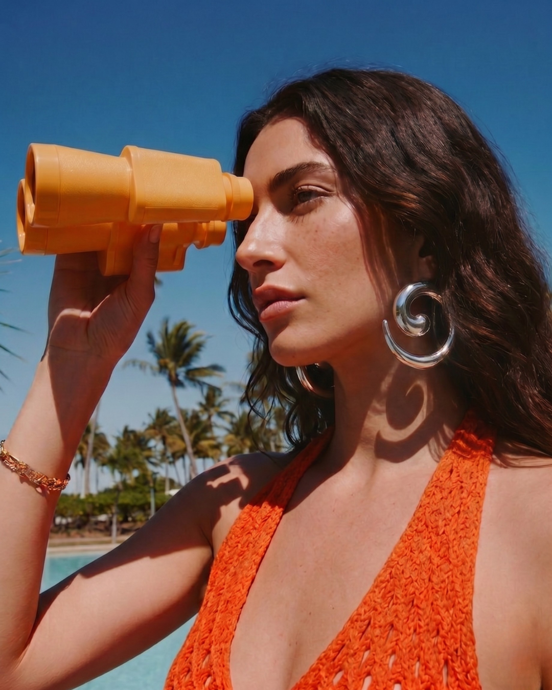 Model wearing silver statement earrings by the pool with summer outfit, bold jewellery styling