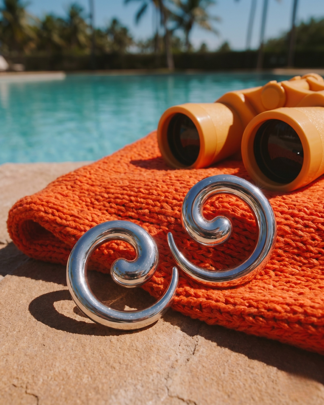 Silver statement earrings placed poolside with summer accessories, modern jewellery styling