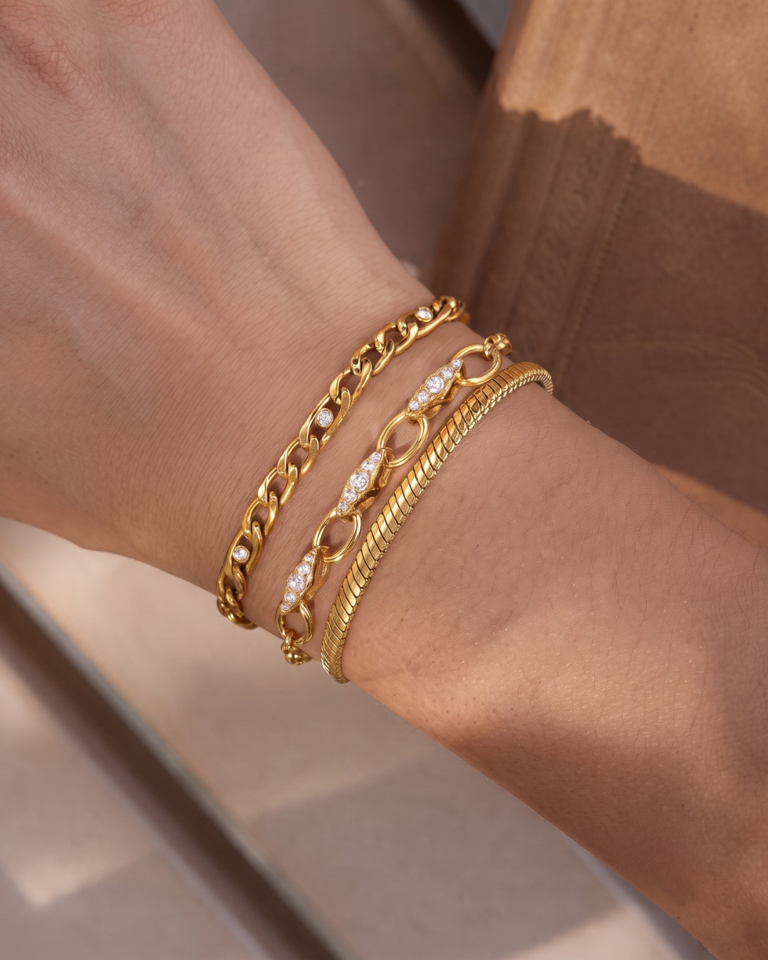 The Wrist Stack styled on the wrist in warm sunlight — three gold-finished bracelets layered together by Clarabelle