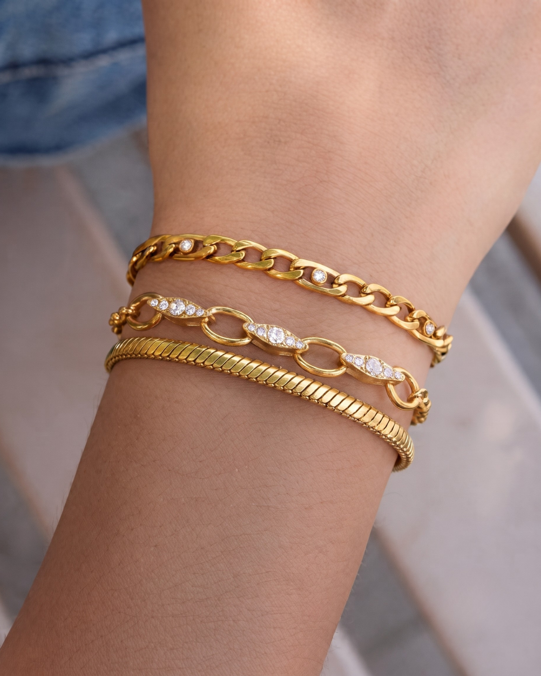 Clarabelle Wrist Stack shown stacked on the wrist — three gold-finished bracelets layered: Marcella Figaro, Chiara pavé rolo, and Lucia snake chain